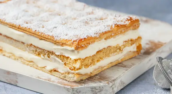 Una deliziosa torta diplomatica, stratificata con soffice crema e sfoglia croccante, spolverata di zucchero a velo.