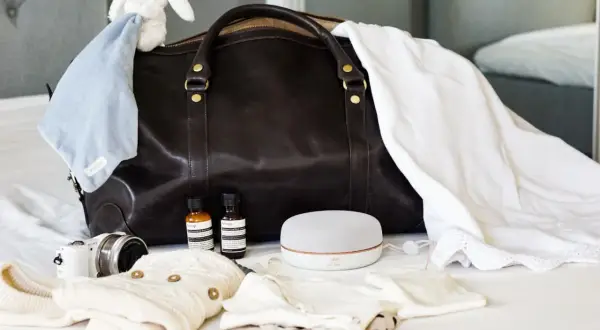 Packlista bb: mörk väska, bebiskläder, nalle, kamera, högtalare och två små flaskor.
