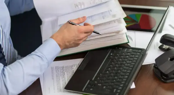 Osoba przegląda dokumenty, na biurku laptop, kalkulator i wykres kołowy. To może być pomocne przy wypełnianiu karty podatkowej.