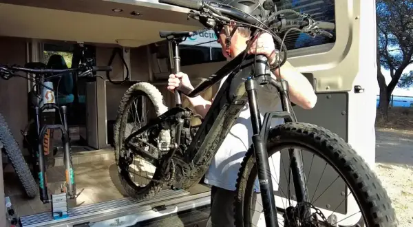 Hombre cargando una bici eléctrica en una furgoneta. Así es como llevar la bici dentro de la furgoneta para tus aventuras.