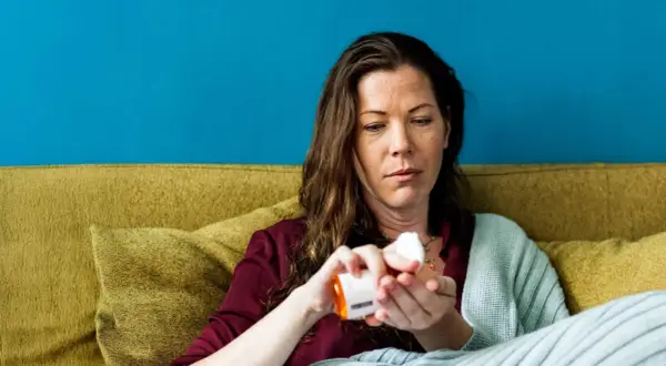 Vrouw neemt medicatie, hopend dat werkt bachbloesem echt. Ze zit op een bank met een deken.