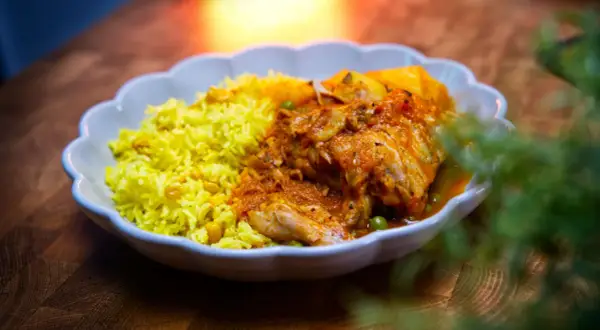 Herzhaftes Sudado de Pollo mit gelbem Reis und Erbsen, serviert in einer weißen Schale auf einem Holztisch.