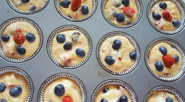 Frisch zubereiteter Teig für Heidelbeer Muffins, mit saftigen Blaubeeren und roten Beeren in einer Muffinform.