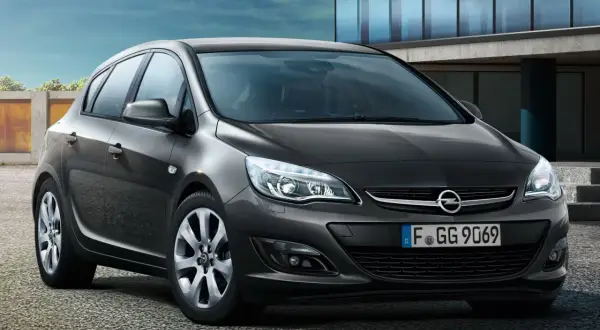 Ciemnoszary Opel Astra J lift z tablicą rejestracyjną F GG 9069 stoi przed nowoczesnym budynkiem.