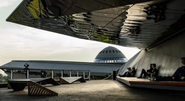 Nowoczesna architektura i nietypowe atrakcje Katowice: ludzie odpoczywają pod futurystycznym zadaszeniem, w tle kopuła Muzeum Śląskiego.