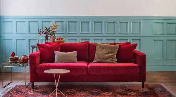 Ein rotes Samtsofa mit braunen Kissen vor einer blau getäfelten Wand. Welche Farbe passt zu Rot? Braun und Blau sind eine tolle Wahl!