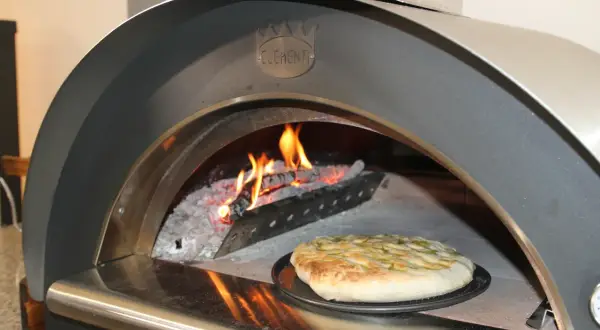 Una crescia dorata pronta per essere infornata in un forno a legna Clementi, con fiamme vive che creano l'atmosfera perfetta per la ricetta.