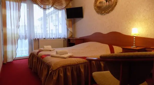 Przytulny pokój w pensjonacie Angela Łeba. Łóżko z czystymi ręcznikami, obraz z końmi i lampka nocna.