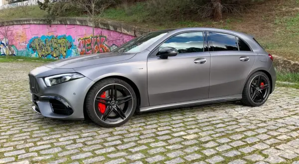 A45 AMG CV gris mate, con pinzas rojas y llantas negras, aparcado sobre adoquines frente a un muro con grafitis.