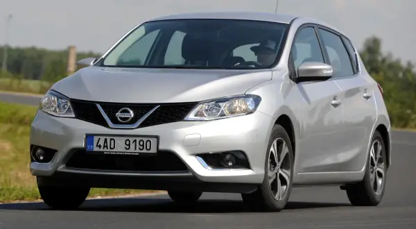 Srebrny Nissan Pulsar w ruchu drogowym. Kierowca w kapeluszu za kierownicą. Wiele pozytywnych nissan pulsar opinie.
