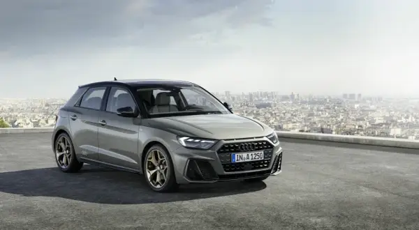 Szary Audi RS1 z brązowymi felgami stoi na dachu z widokiem na miasto.