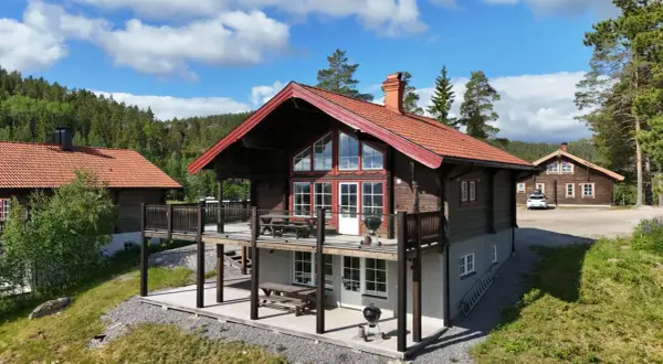 Träfasade hus med röda tak och stora fönster, belägna i en skogsmiljö. En härlig plats att bo på, kanske vid alpstigen i Järvsö.