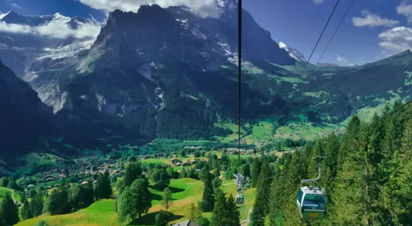 Widok z kolejki linowej na dolinę Grindelwald, z górami w tle i zielonymi łąkami.