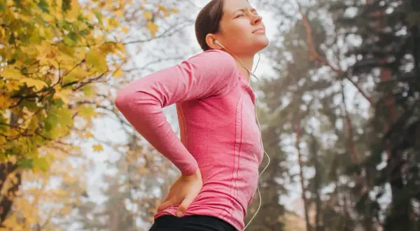Femme en tenue de sport, le dos douloureux, se tenant la hanche. Le sport peut être mauvais pour le dos.