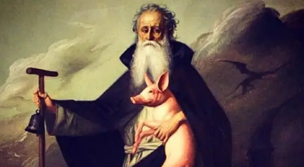 Un anziano barbuto con un maialino rosa, un bastone con campana e un'ombra di drago. La storia del porcellino di Sant'Antonio.