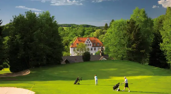 Zwei Golfer auf dem grünen Rasen des Golfclubs Schloss Georghausen, im Hintergrund das malerische Schloss.