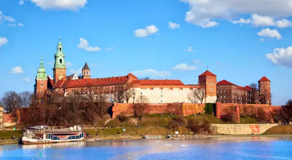 Majestatyczny Wawel góruje nad Wisłą. Widok na wejście na Wawel z rzeki, z widoczną barką i błękitnym niebem.