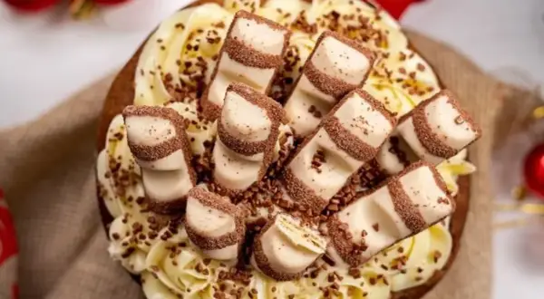 Tarta decorada con crema amarilla y trozos de tarta kinder bueno, espolvoreada con virutas de chocolate.