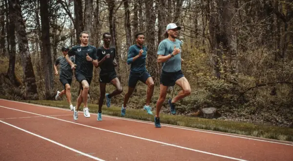 Cinq coureurs s'entraînent sur une piste, leurs foulées rythmées par un entraînement de fractionné course intense.
