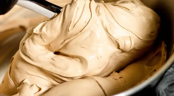 Gładka, kremowa masa o kolorze **salted caramel** jest mieszana łopatką w metalowej misce.