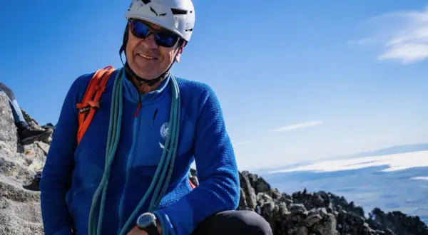 Uśmiechnięty alpinista w kasku i okularach przeciwsłonecznych, gotowy na wejście na Gerlach. Liny i plecak świadczą o jego pasji.