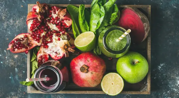 Frische Zutaten für eine **Detox Kur**: Granatapfel, grüner Saft, Rote Bete, Äpfel und Limetten in einer Holzkiste.