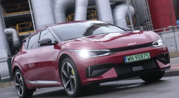 Czerwone Kia EV6 z zieloną tablicą rejestracyjną na tle przemysłowych rur.