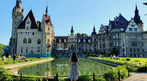 Kobieta podziwia zamek Moszna, jedną z najpiękniejszych atrakcji turystycznych Polski, z malowniczym stawem w tle.