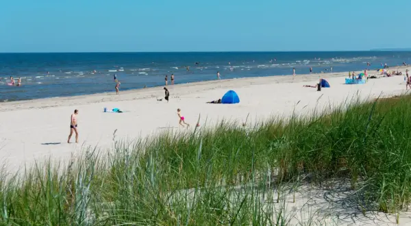 Menschen genießen einen sonnigen Tag am Strand der Ostsee. Nach der Fahrt mit dem Zug von Berlin ist dies eine willkommene Erfrischung.