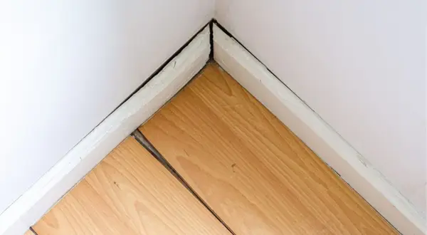 Esquina de habitación con suelo laminado hinchado por agua, mostrando las tablas separadas y levantadas.