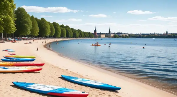 Färgglada kajaker på stranden vid en av Stockholms badplatser. Människor badar och paddlar i det blå vattnet med stadens silhuett i bakgrunden.