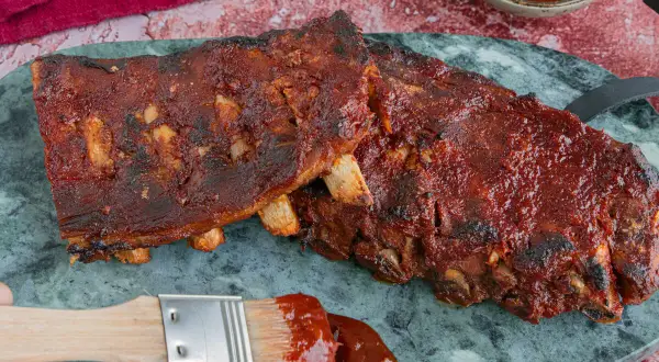 Saftige Spareribs sous vide, glasiert mit BBQ-Sauce. Ein Pinsel mit Sauce liegt daneben.