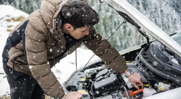 Un homme en doudoune vérifie le moteur de sa voiture sous la neige. Une astuce pour démarrage à froid diesel peut l'aider.