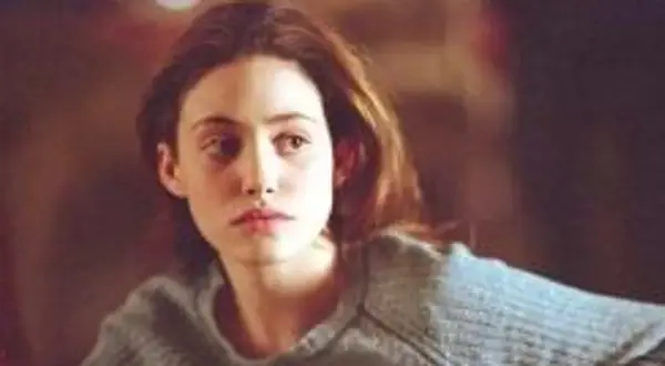Emmy Rossum w szarym swetrze, aktorka znana z filmów, seriali i programów, zamyślona.