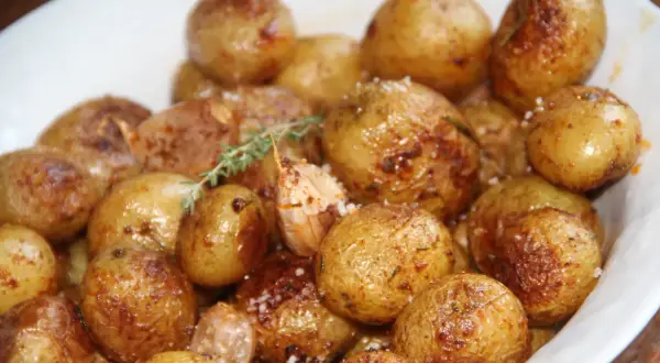 Un plat de pommes de terre grenaille au four, dorées et croustillantes, parsemées de sel et d'herbes.