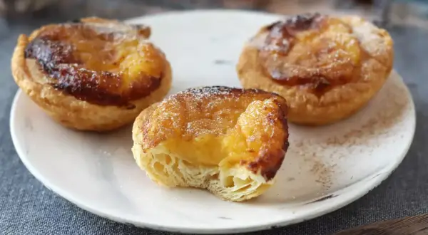 Tre gyllene pastel de nata med krämig fyllning och karamelliserad yta, pudrade med florsocker.