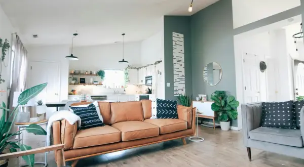 Wygodny salon z dwoma sofami zamiast narożnika, brązową i szarą, ozdobiony roślinami i geometrycznymi poduszkami.