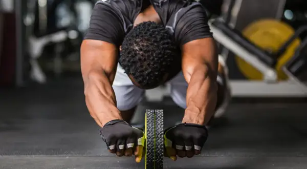 Man gör en ab wheel rollout i gymmet, med fokus på magmusklerna.