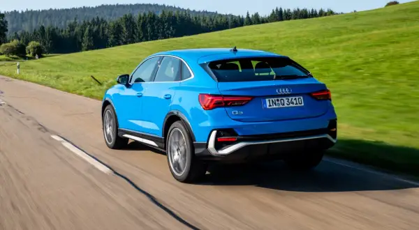 Niebieskie Audi Q3 Sportback jedzie po krętej drodze wśród zielonych wzgórz. Poznaj jego wymiary.