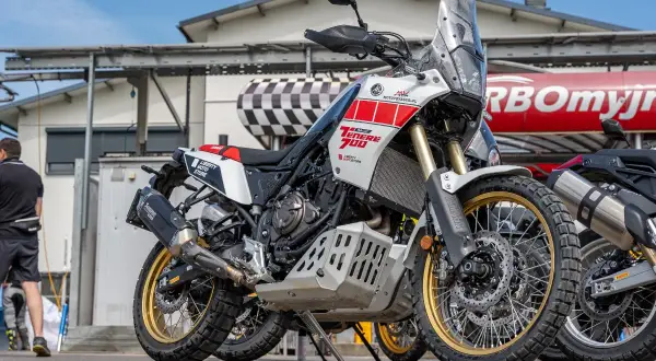 Biało-czerwony motocykl Yamaha Ténéré 700 z złotymi felgami, zaparkowany na zewnątrz.