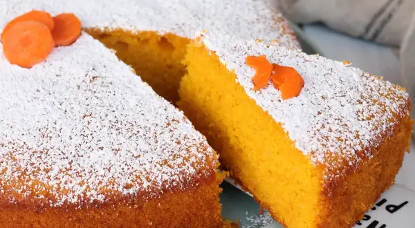 Una fetta di torta Camilla, soffice e arancione, cosparsa di zucchero a velo e decorata con carote.