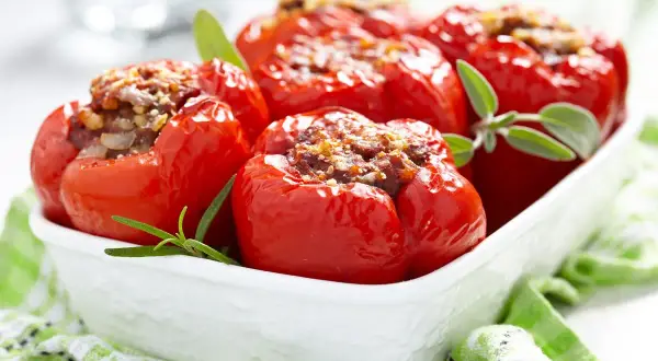 Peperoni ripieni di carne, cotti al forno e guarniti con erbe aromatiche, serviti in una ciotola bianca.