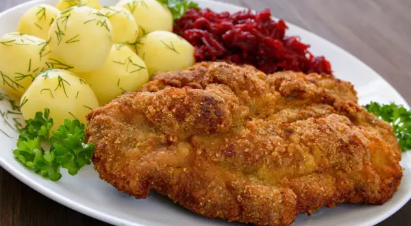 Kotlet schabowy w panierce z ziemniakami i buraczkami na białym talerzu.
