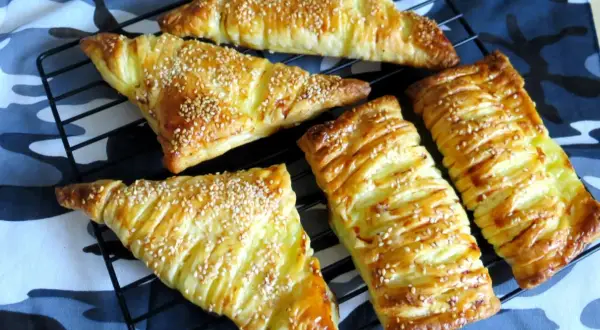 Chrupiące ciasto francuskie z serem, posypane sezamem, prezentuje się apetycznie na czarnej kratce.