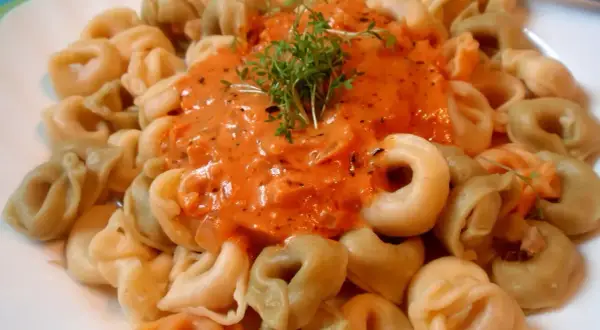 Kolorowe tortellini w kremowym sosie pomidorowym, udekorowane świeżą rukolą. Pyszny sos do tortellini kusi aromatem.