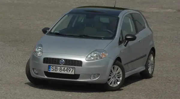 Srebrny Fiat Grande Punto z czarnym dachem i nowymi żarówkami, gotowy do jazdy po brukowanej nawierzchni.