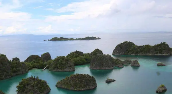 Grüne Inseln ragen aus türkisfarbenem Wasser, eine malerische Aussicht, die man vom Raja Ampat Flughafen aus genießen kann.