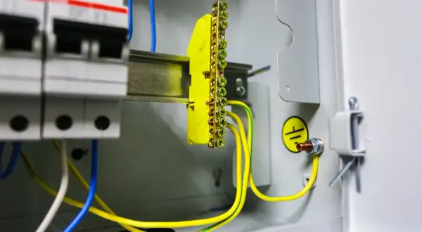 Wnętrze rozdzielnicy elektrycznej z widocznym żółtym listwą zaciskową i przewodami, symbolizującymi pomiar rezystancji uziemienia.
