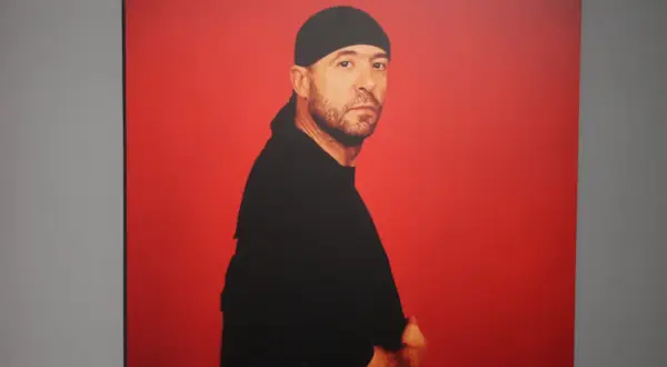 Retrato de Manuel Piña con gorro y camiseta negra, sobre fondo rojo vibrante.