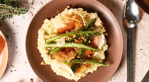 Un crémeux risotto aux asperges vertes, garni de copeaux de parmesan et de fines tranches de prosciutto. Une recette parfaite pour un repas printanier.